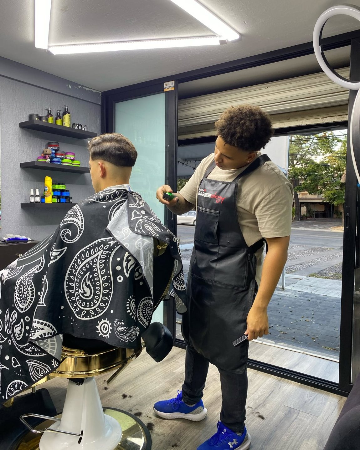 Barbero de Los Dominican perfilando el fade de un cliente junto al ventanal de la barbería