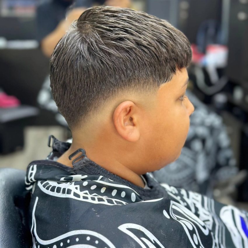 Niño con taper fade terminado y la parte de arriba peinada al frente