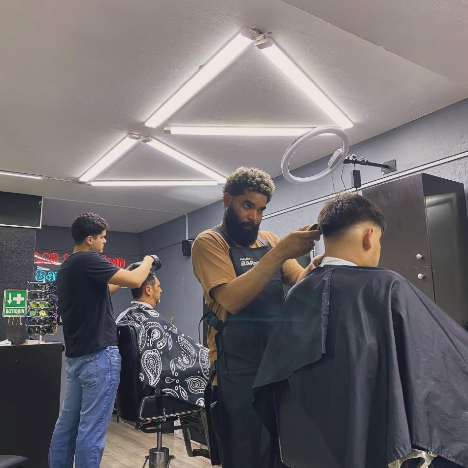 Dos barberos atendiendo a dos clientes al mismo tiempo en las estaciones de la barbería