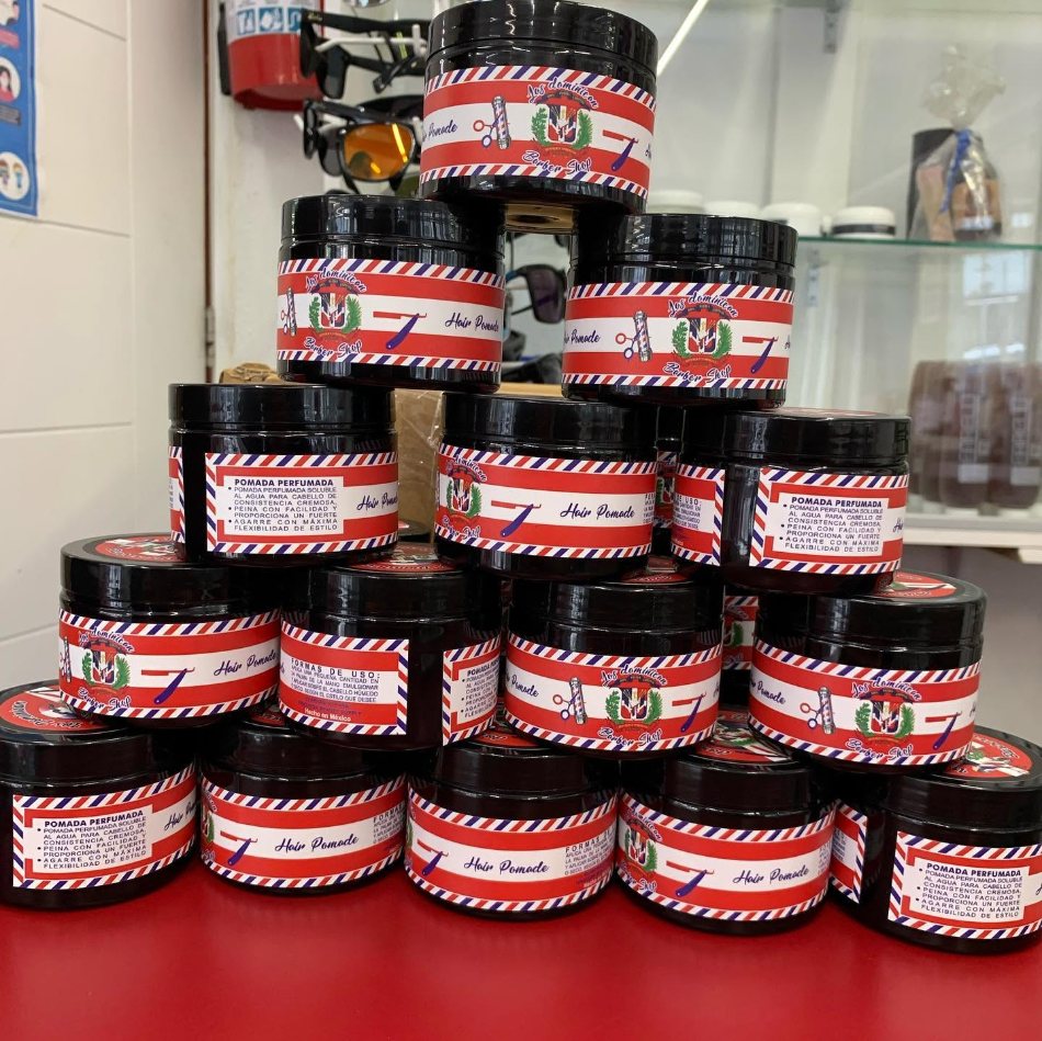 Pirámide de frascos de la pomada perfumada Los Dominican Barbershop sobre el mostrador rojo